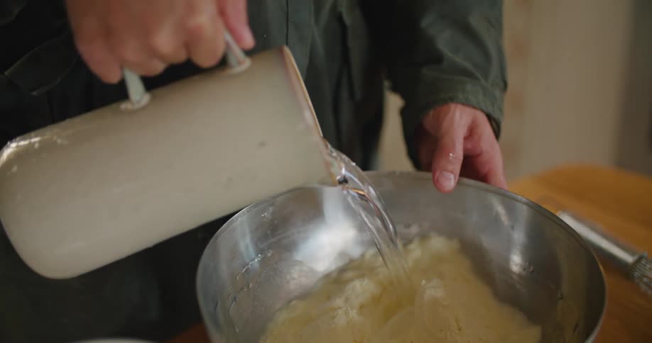A person pours water into a bowl of flour