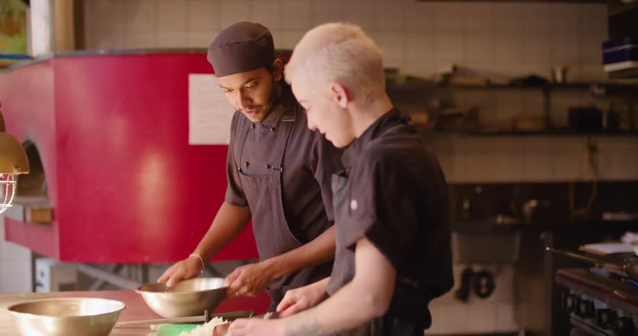 Two chefs laugh and talk as they prepare food in a restaurant
