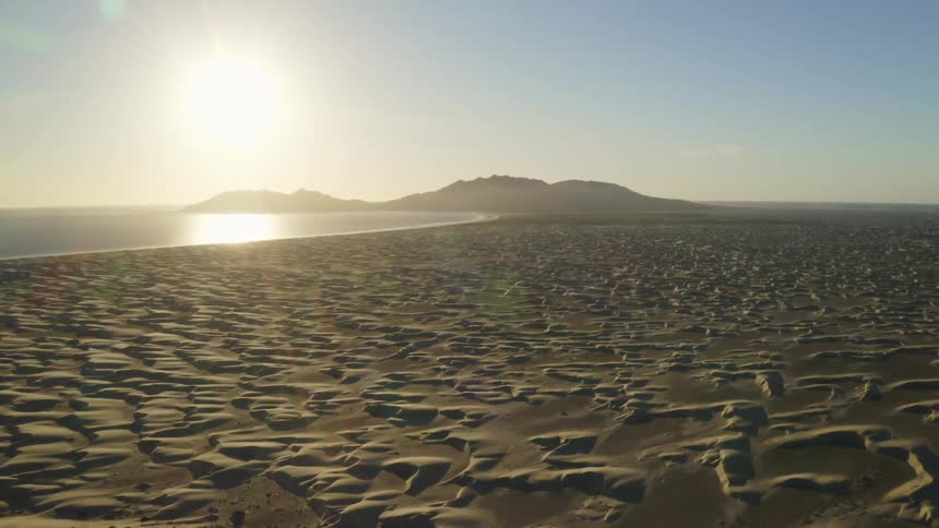 Sand dunes on the coastline next to the ocean at sunset
