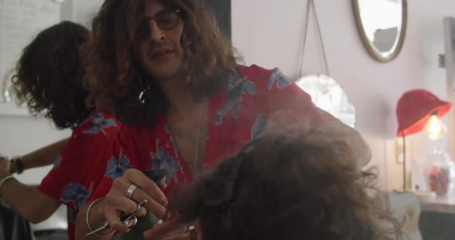 A hair stylist sprays something on the hair of the client in front of him
