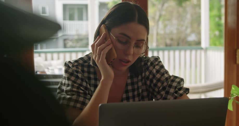 A woman sits in front of a laptop and talking on the phone