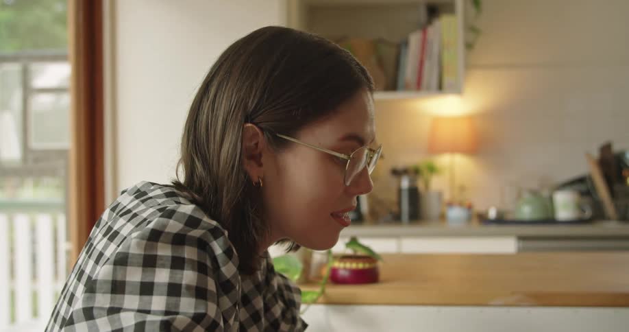 A woman laughs while typing on her laptop while sitting at her kitchen table
