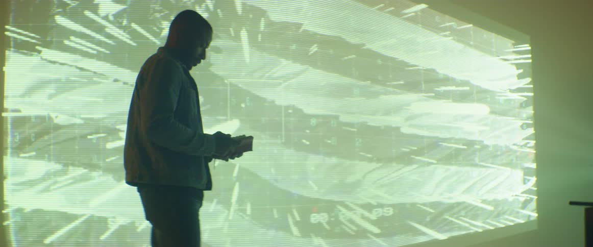A man standing in front of a large screen with a movie playing looks at his cell phone