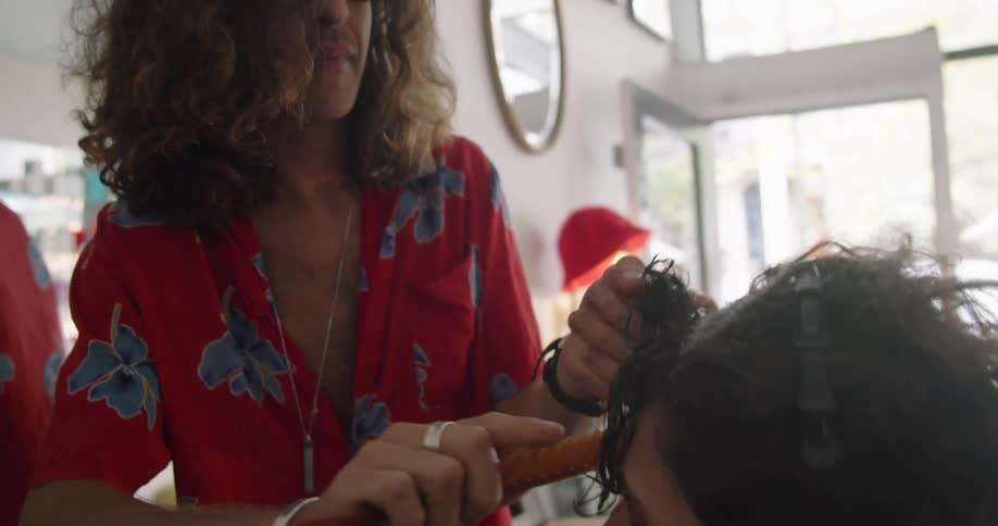 A hair stylist comb the hair of a woman who is sitting in a chair inside of a shop