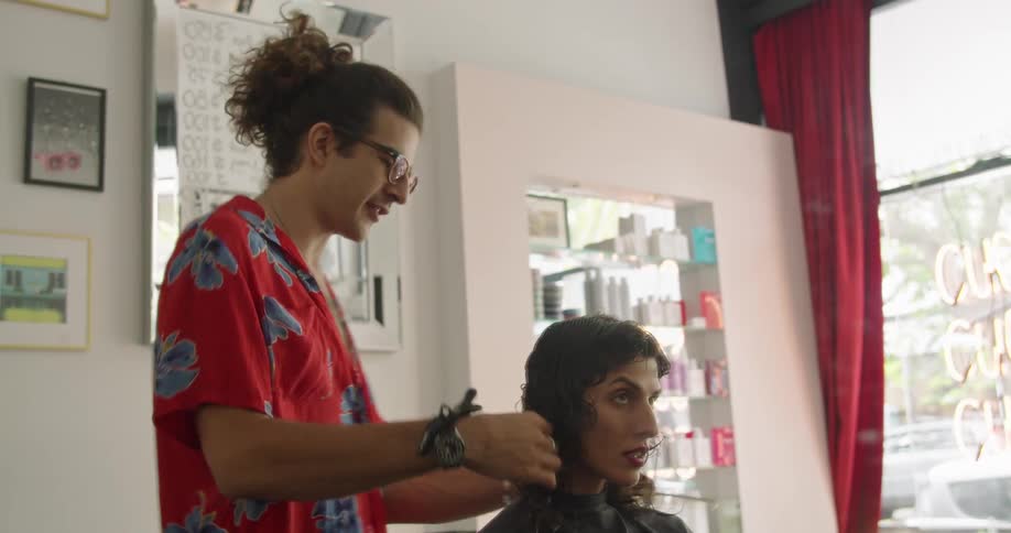 A hairstylist combs the hair of a woman sitting in a chair inside of a beauty salon