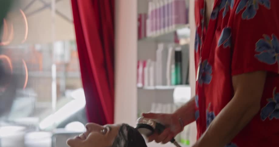 A hair stylist washes and rinses the hair of the client in the wash bowl