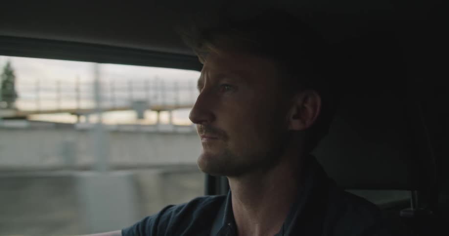 Side view of a man with a polo shirt driving a vehicle on the city highway
