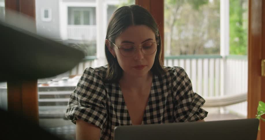 A woman sits and types on her laptop near a door leading to a large outdoor patio