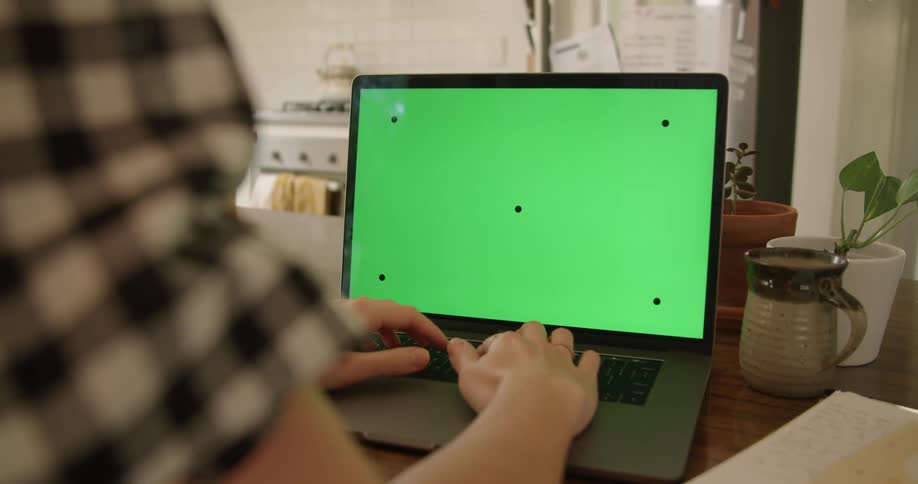 Woman with a plaid shirt sits at table and works on macbook laptop in the kitchen