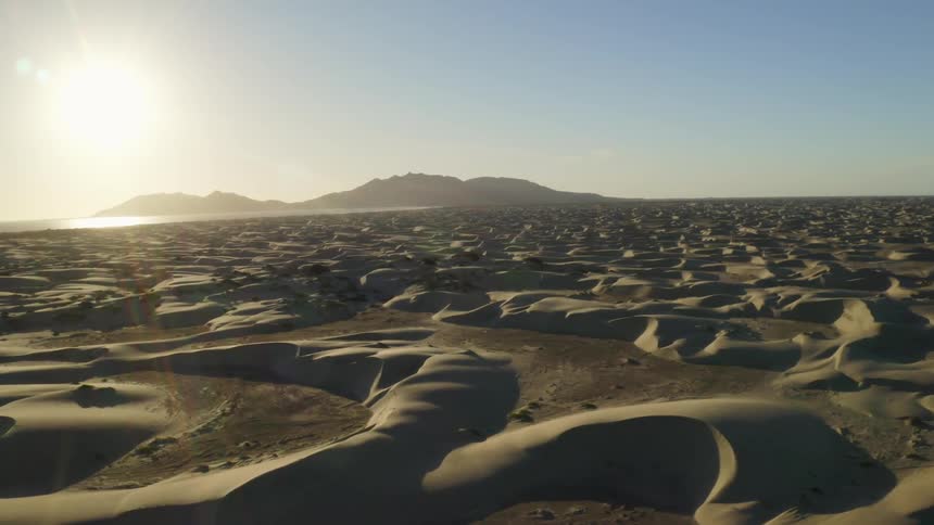 A desert with sand dunes with the sun the sky and clouds in the background
