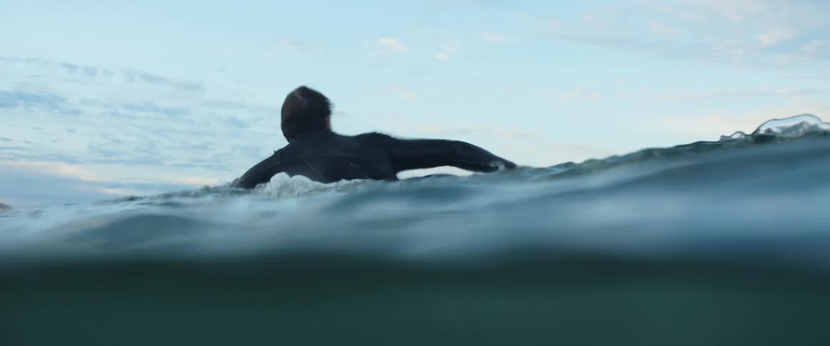 Man wearing a diving suit swims with a surfboard at dusk