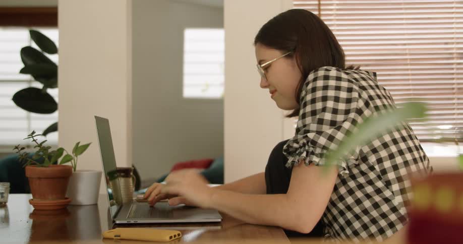 A teenage girl sits at home and types on her laptop