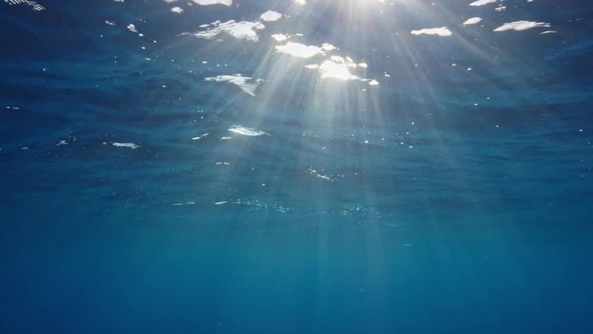 Beams of sunlight sparkle and radiate beneath the ocean surface as waves rolls above
