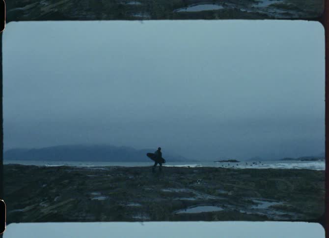 Silhouette of a person carrying a surfboard on the coast on an overcast day