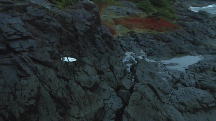 Young man holding a surfboard walking on the rock promontories in front of the coast