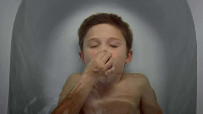 A young boy pinching his nose and submerging his head in a bathtub