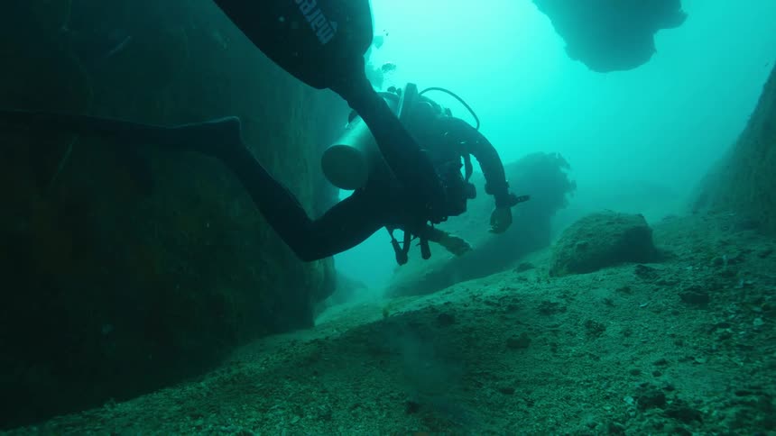 A scuba diver in full scuba equipment swimming underwater in the ocean
