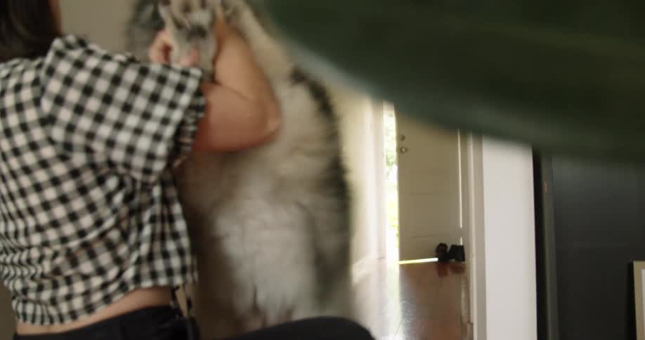 A woman with glasses playing with a dog with a wall and door in the background