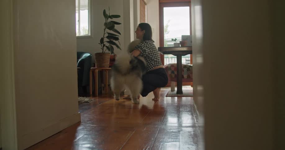 A woman kneels on the floor and her dog comes running to her arms