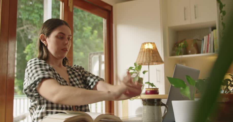 A woman stretches her arms while studying and goes back to using her laptop