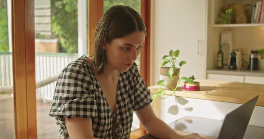 A woman in a room sitting at a table typing on a laptop with a door in the background