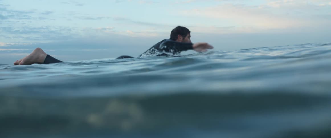 Man wearing a black wet suit swimming over a surfboard in the ocean