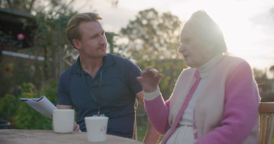 A young man sits outside and talks with an elderly woman