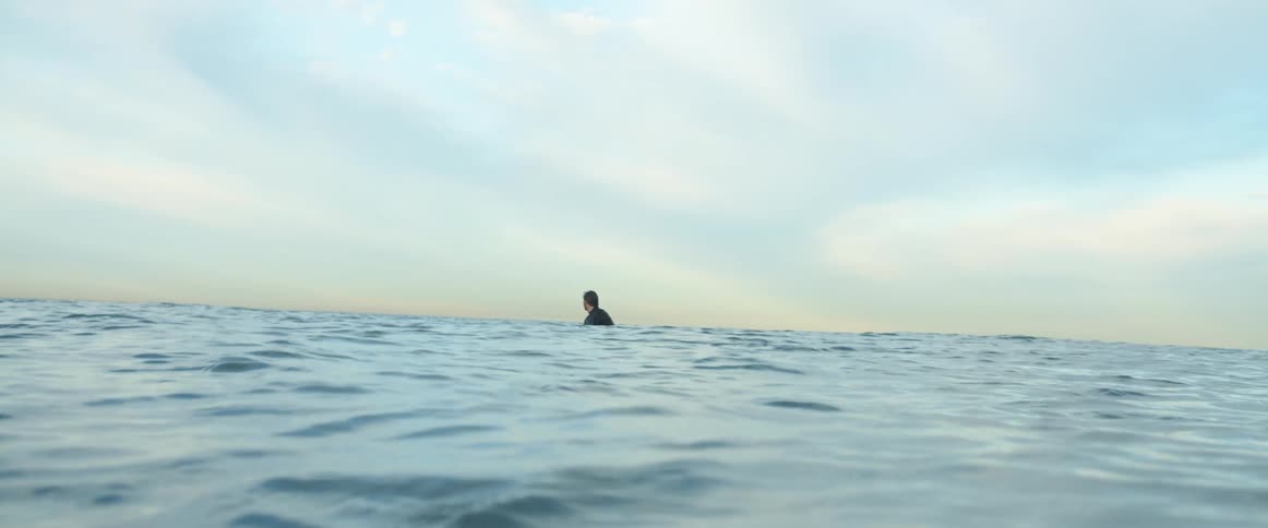 A man in the ocean standing in water with the sky and clouds in the background