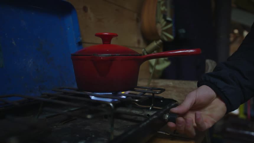 A person putting a red pot onto a lit burner on a gas stove