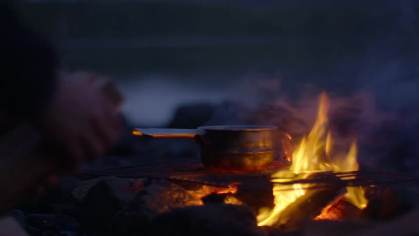 A man chopping wood next to a burning campfire at night