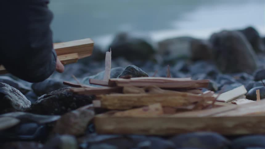 A person cutting firewood with an ax outside on rocky ground