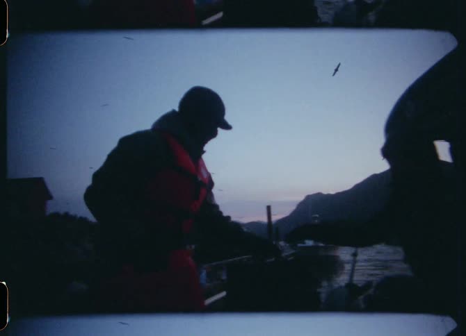 A man steps off a boat and hands a cooler bag to a man on another boat