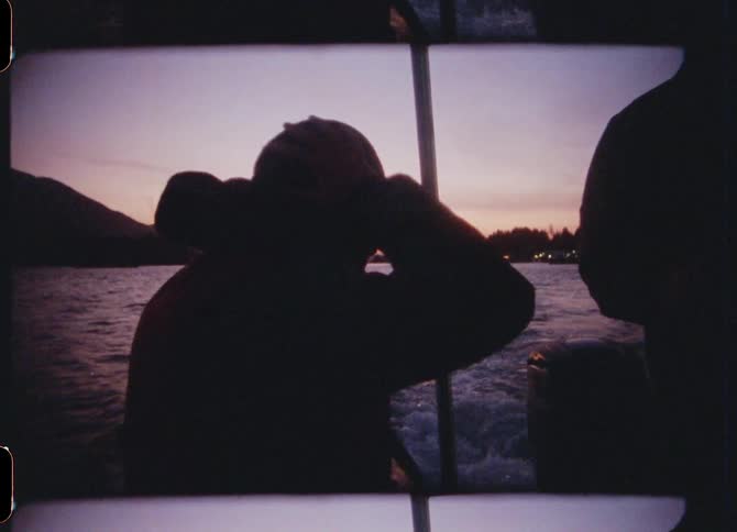 Silhouette of a man adjusting his hat while riding a boat on a lake at sunset