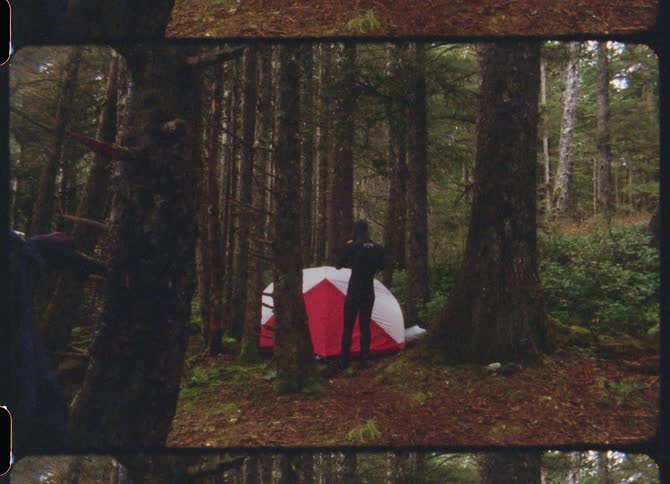 Man with a diver suit stands next to a white red tent in the woods