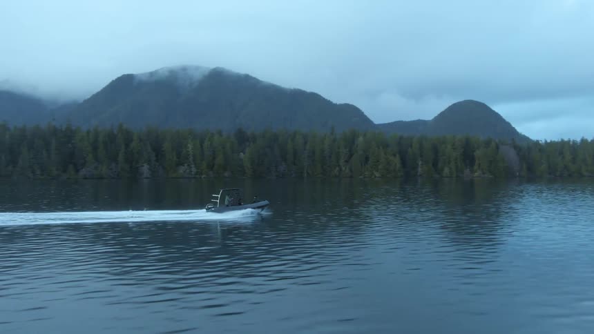Boat navigating on the calm water of a lake near the pine tree forest on the mountains