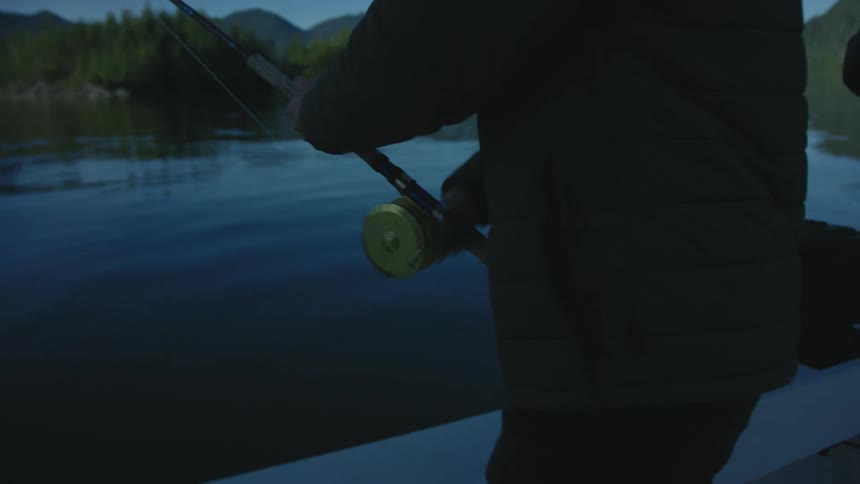 A man is on a boat and fishing on the lake