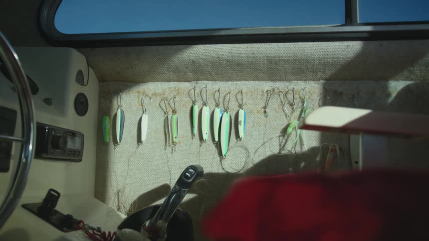 A boat with the steering wheel a chair fishing hooks and a window