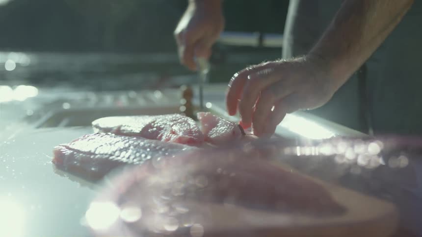 A fisherman cleans and slices fish on his boat on the water