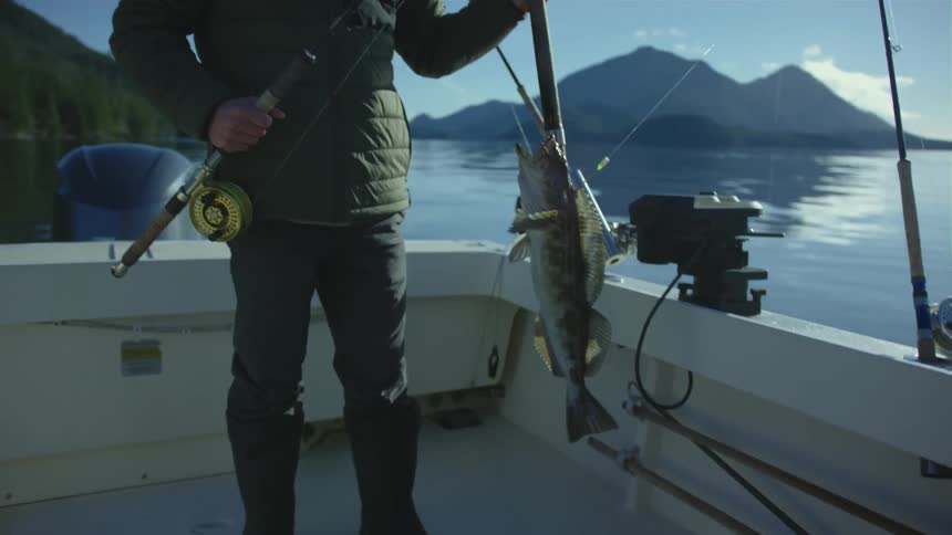 A man stands on a boat and holds his fishing rod with a fish on it