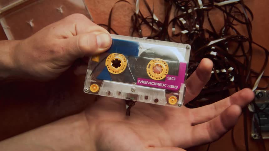 A man uses his pinky finger to re thread a broken cassette tape