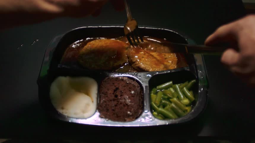 A person sitting at a table and using a knife and fork to cut food