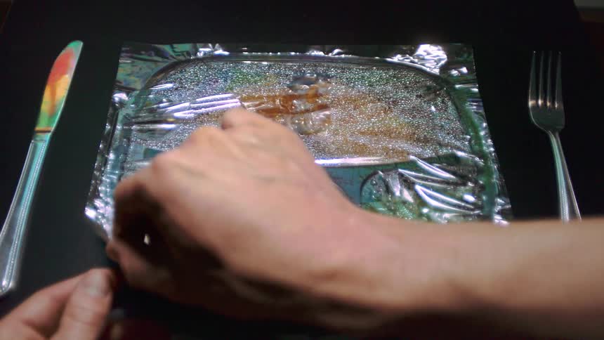 Person peels back plastic from heated frozen dinner