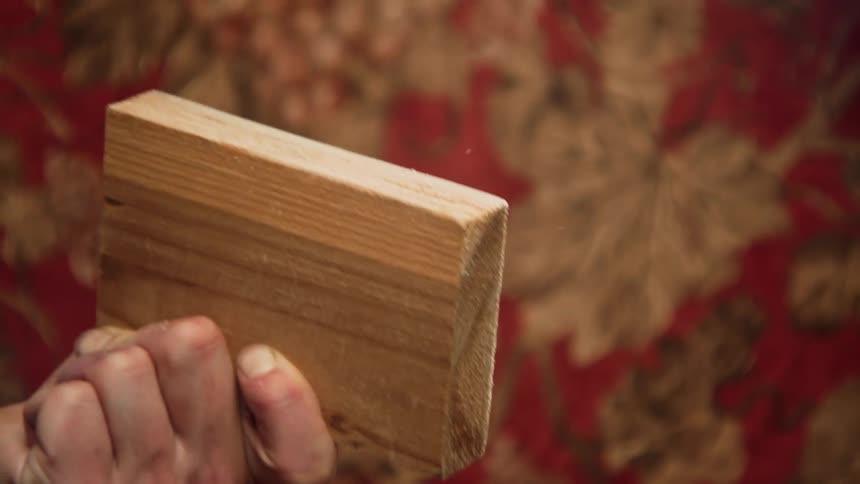 A person uses sand paper to sand a block of wood