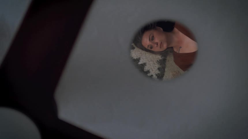 A womens reflection is shown in a round mirror on the ceiling as she lies down below a fan