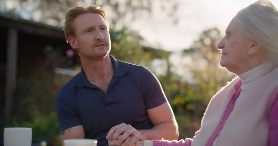 A man and a woman sitting at a table with trees the sky and clouds in the background
