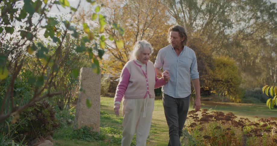 Elderly woman and middle aged man holding hands wanders around the garden