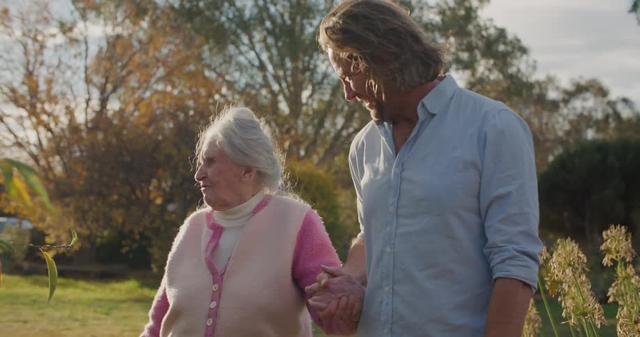 Son helping holding his elderly grandmother’s hand while walking in the yard