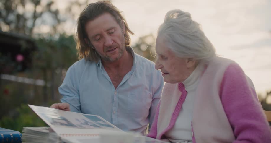 A man and a woman looking at an album with trees the sky and clouds in the background