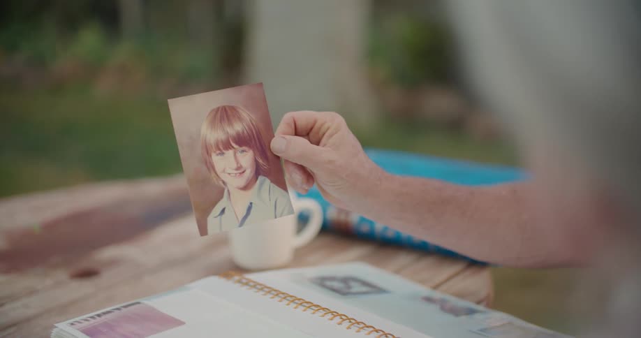 Middle aged man hand holds up a foto in order elderly woman to see in the garden