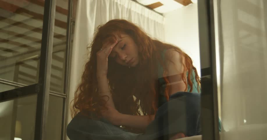 A tired red headed girl rubbing her forehead with her eyes closed